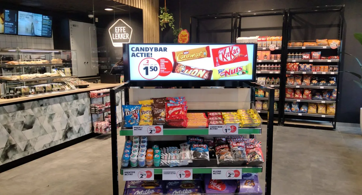 Ondernemer met bezoekerspasje, armen over elkaar, in een gangpad met assortiment